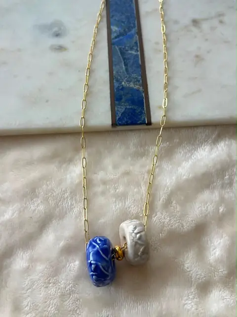 Cadena dorada fina con un dije azul y blanco