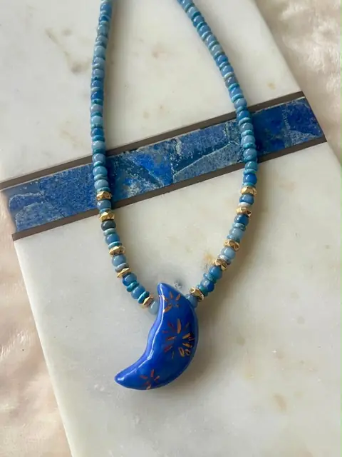 Collar de cuentas azul claro con una luna azul, sobre mármol