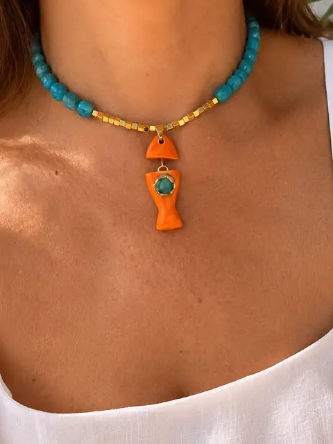 Collar de cuentas turquesa con un pez de cerámica naranja, puesto sobre una blusa blanca