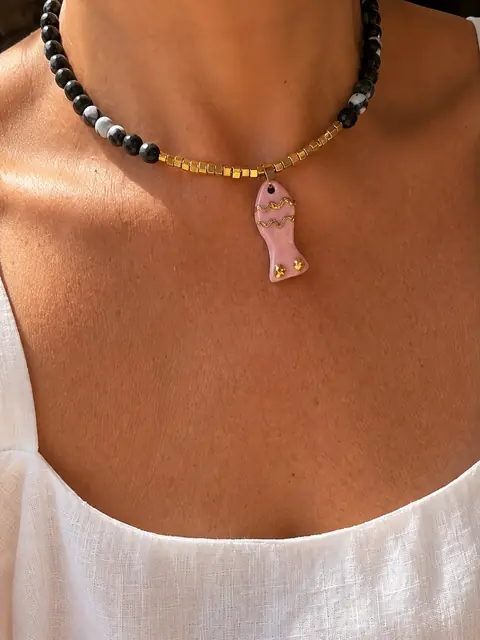 Collar de cuentas negras y blancas con un pez de cerámica rosa, puesto