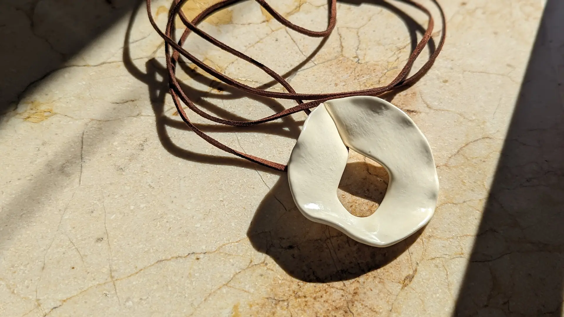 Collar de cerámica blanca con cordón de cuero sobre mármol, al sol