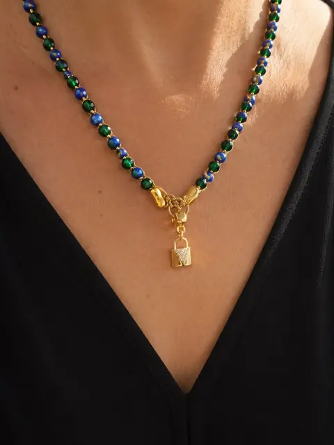 Collar de cuentas azules y verdes con un candado dorado, sobre ropa negra